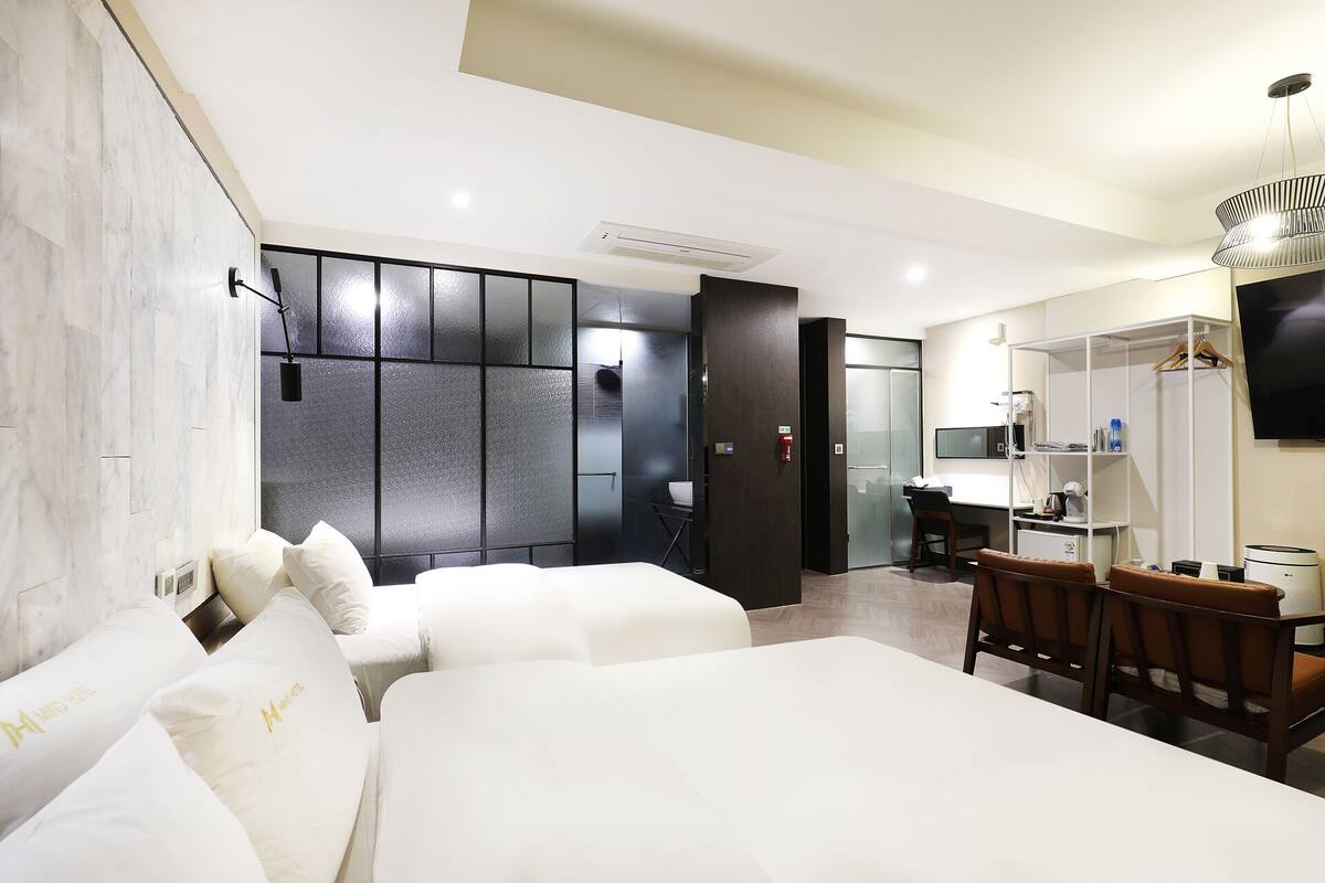 A modern hotel room with a large bed, a desk, a chair, a wardrobe, and a television.