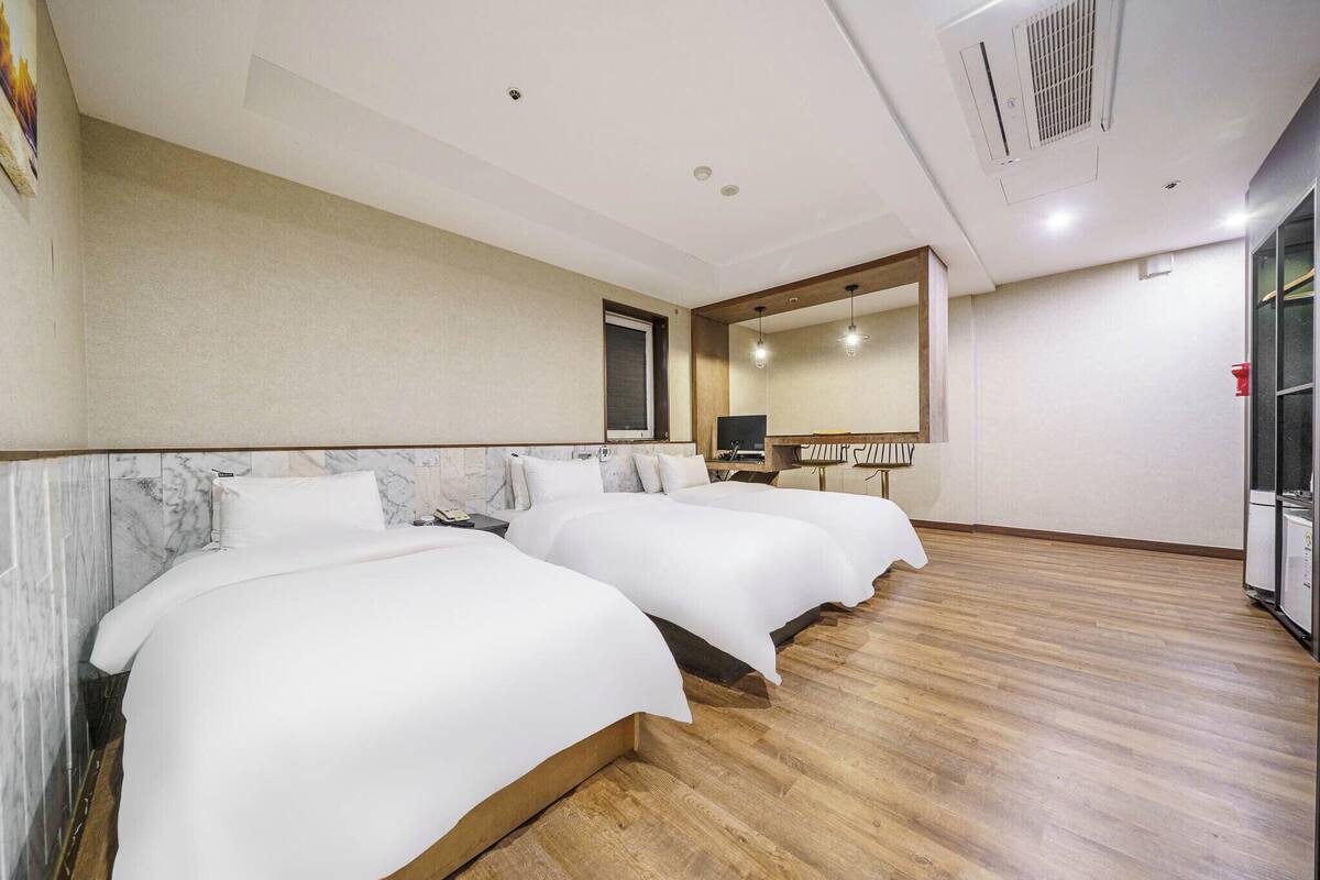 A hotel room with two beds, marble headboard, wooden flooring, a large mirror, and a desk with a computer.