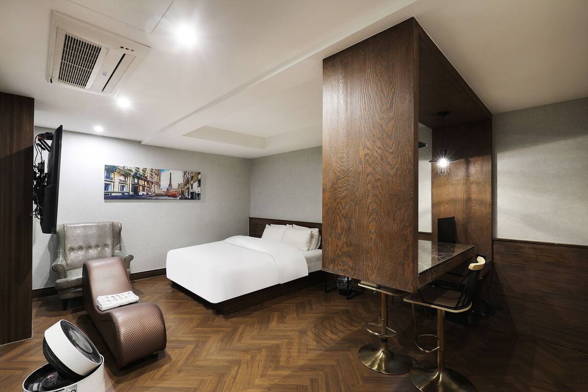 A hotel room with a bed, a chair, a desk, and a mirror.