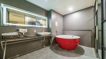 A modern bathroom with a large mirror, a red bathtub, a white sink, and a hairdryer on the vanity.