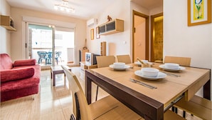 Un comedor con una mesa de madera dispuesta para cuatro personas, un sofá rojo y un televisor sobre un mueble.