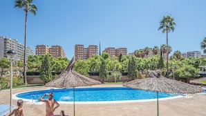 Una piscina con palmeras y un paisaje urbano al fondo.