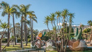 Un parque con esculturas, palmeras y un edificio al fondo.