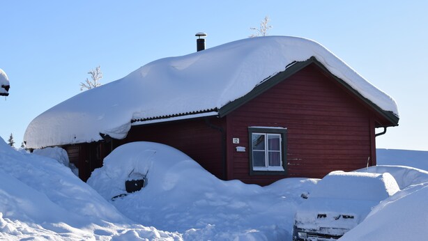 A red wooden cabin covered in snow, with a chimney and a window.