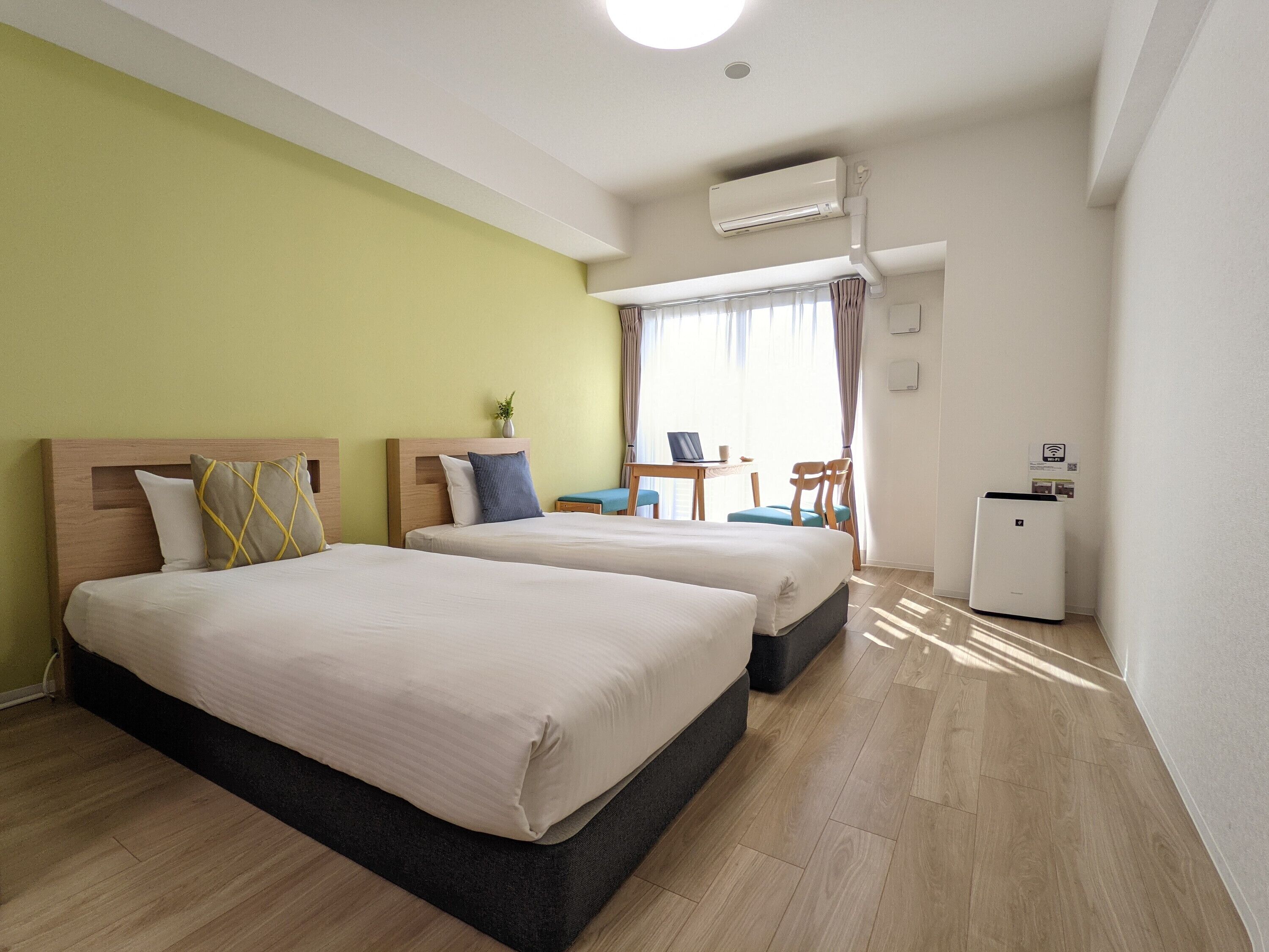 Habitación de hotel con dos camas, un escritorio, una silla y un equipo de aire acondicionado.