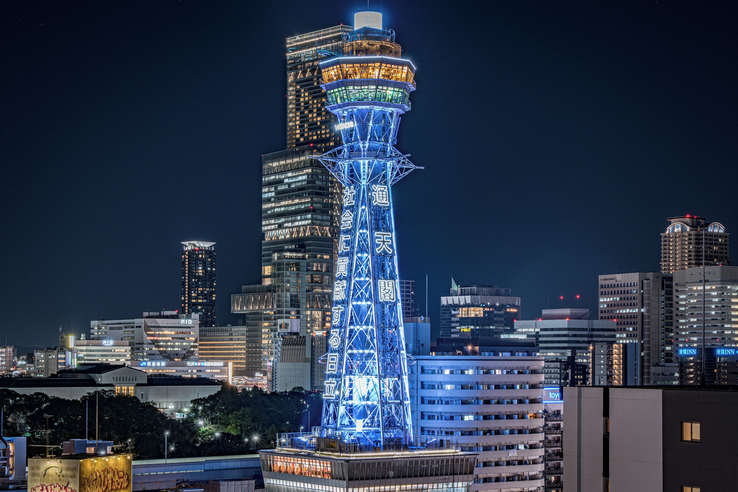 A high-rise building with a prominent tower structure, surrounded by other buildings in a cityscape.