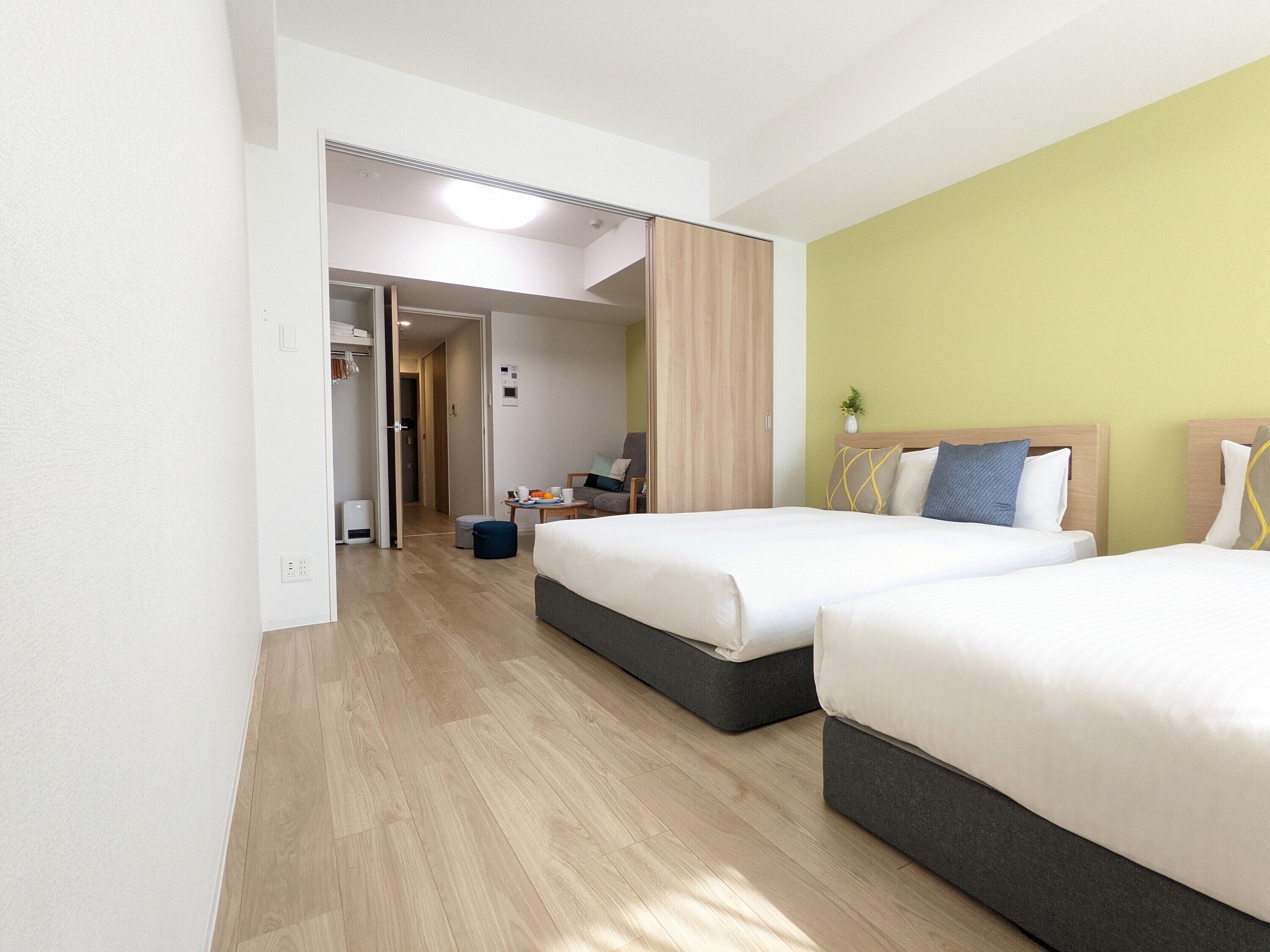 A hotel room with two beds, a desk, a chair, and a small table with a plant.