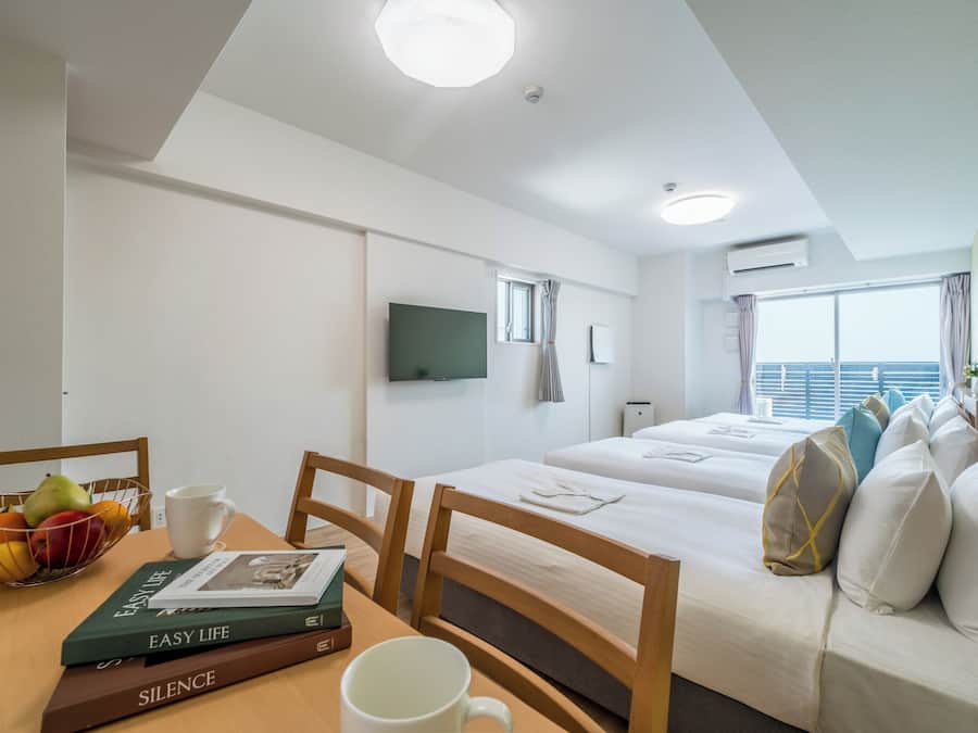Une chambre d’hôtel avec un lit, un bureau avec des livres et une tasse, un téléviseur fixé au mur et une fenêtre donnant sur un paysage agréable.