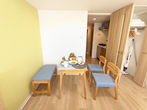 A compact dining area with a table set for two, a bench, and a kitchen in the background.