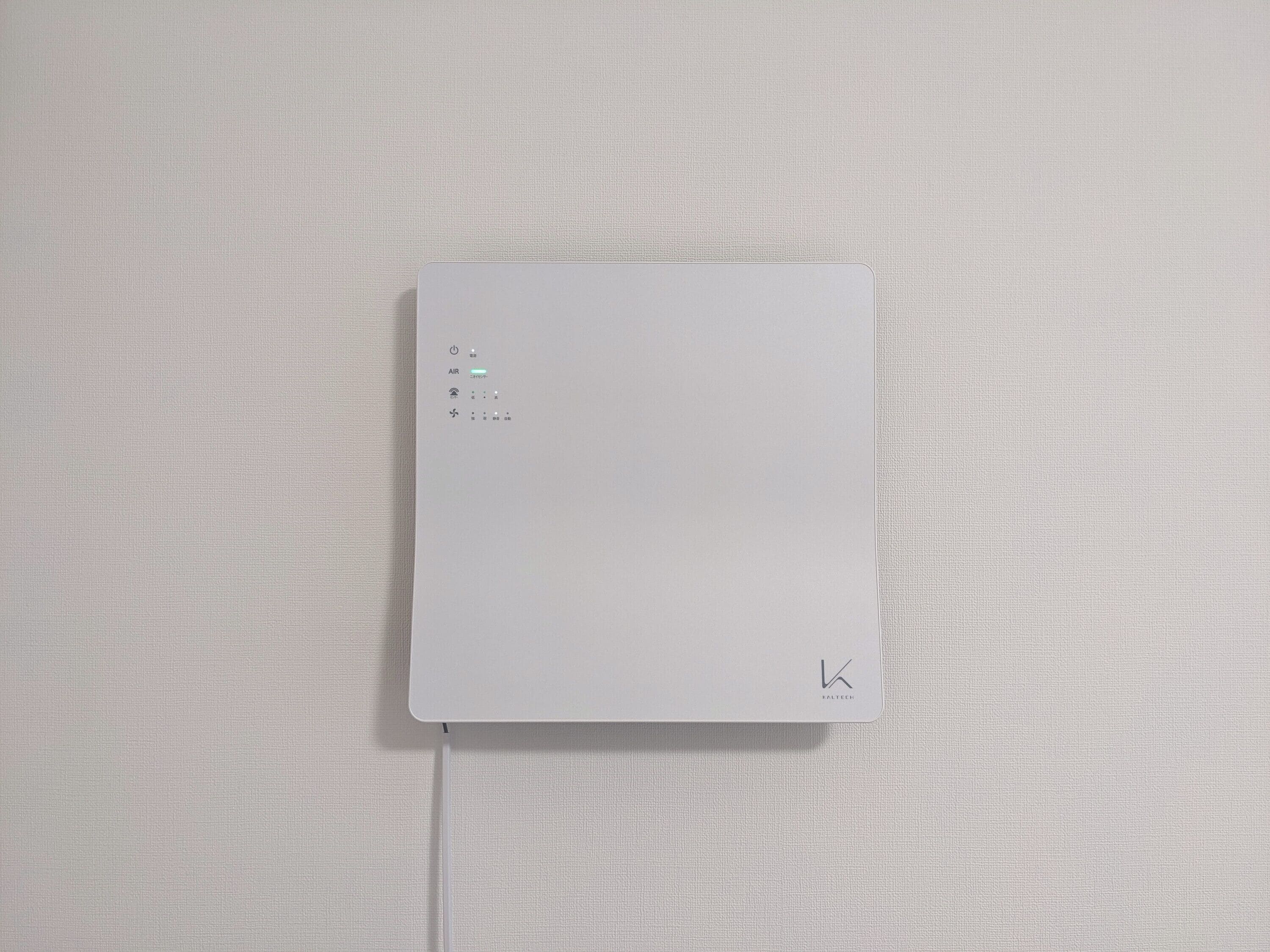 A white electronic device with a power button, an air quality sensor, and a few other controls, mounted on a textured wall.