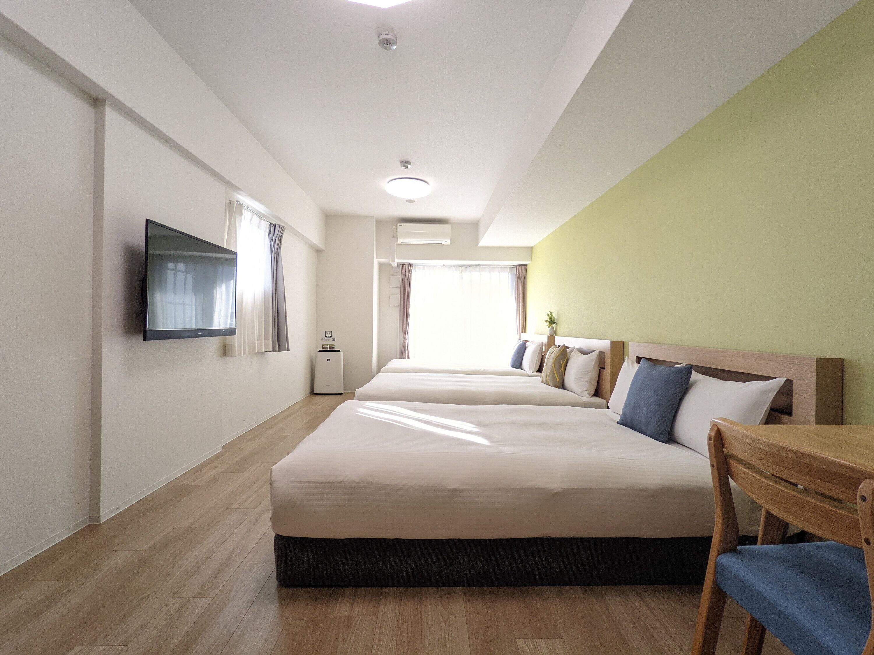 A hotel room with two beds, a TV, a small table, and a window with curtains.