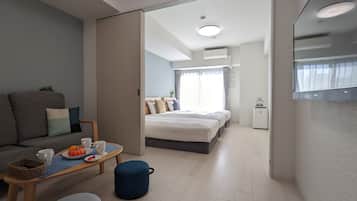 Quarto de hotel moderno com sofá, mesa de jantar com cesta, um banquinho azul e cama com cabeceira.