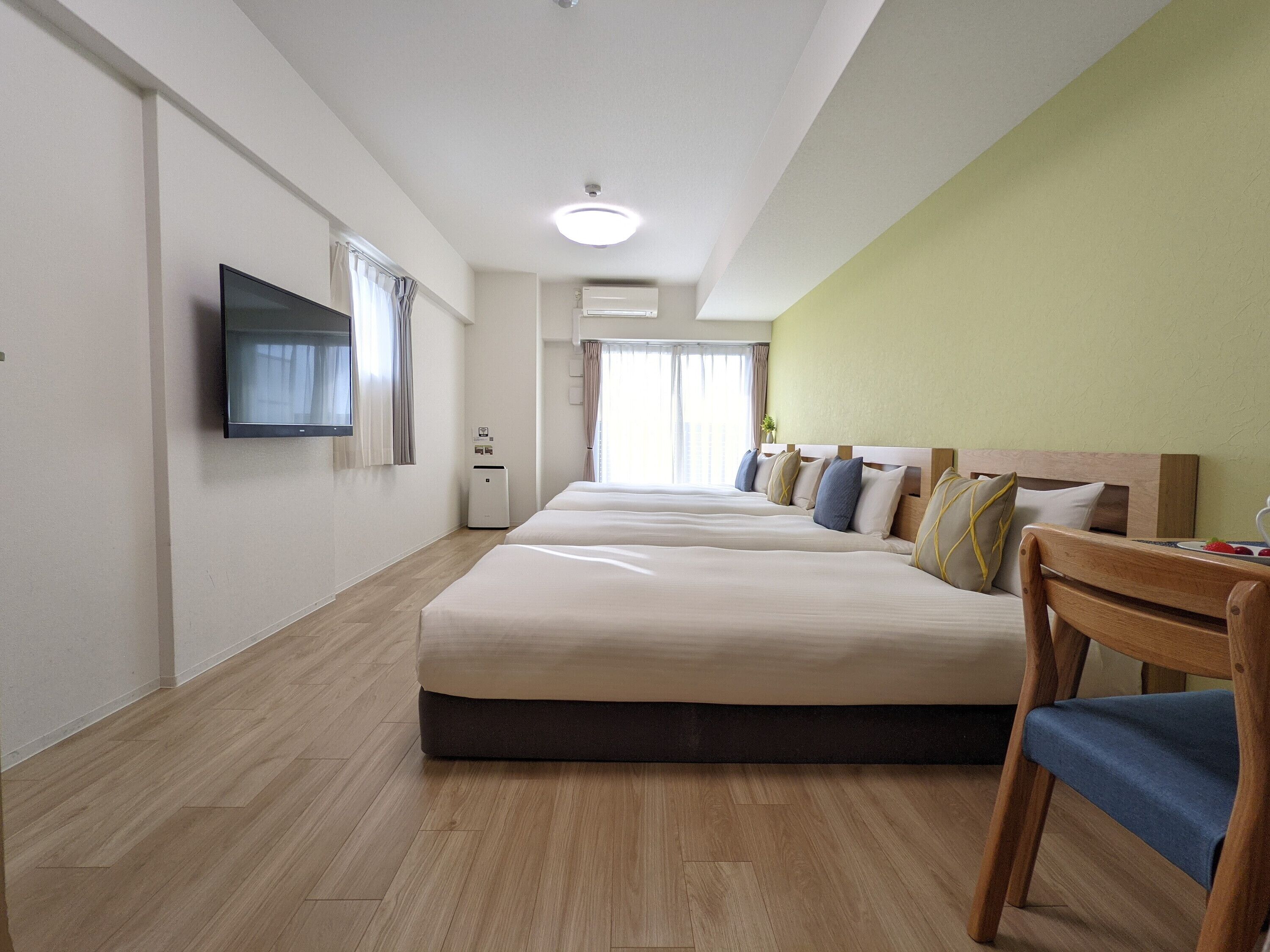 A hotel room with a large bed, a TV, a desk with a chair, and a window with curtains.