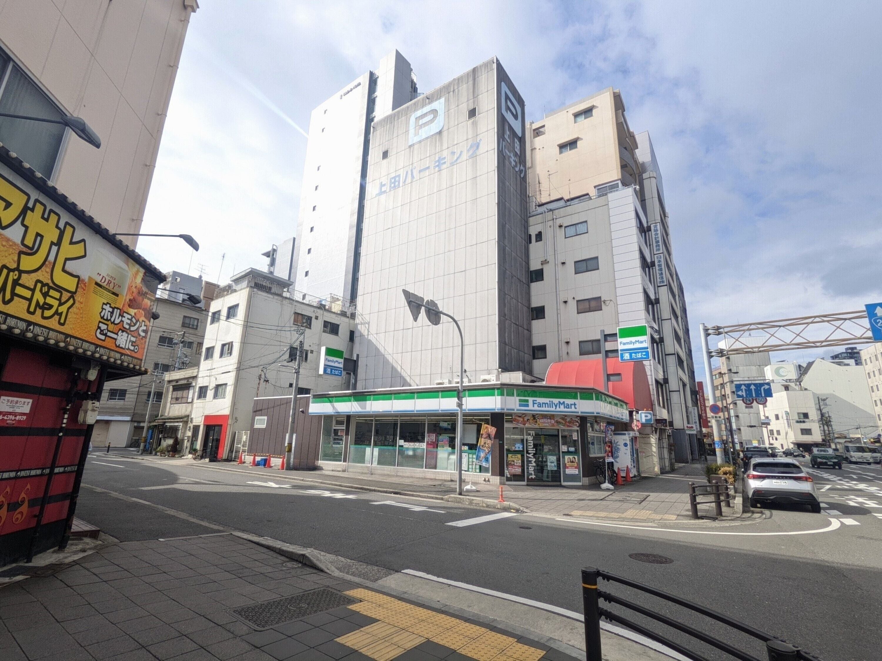 A street view with a FamilyMart convenience store, a tall building with a 'P' logo, and a red storefront with yellow signage.