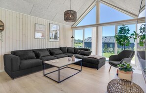 Relax in a spacious room with a large sofa, coffee table, and armchair, offering a view of the surrounding landscape.