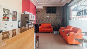 A reception area with a wooden counter, orange sofas, a small table, and a TV mounted on the wall. - OYO 2010 Satria Guest House (Ambon)