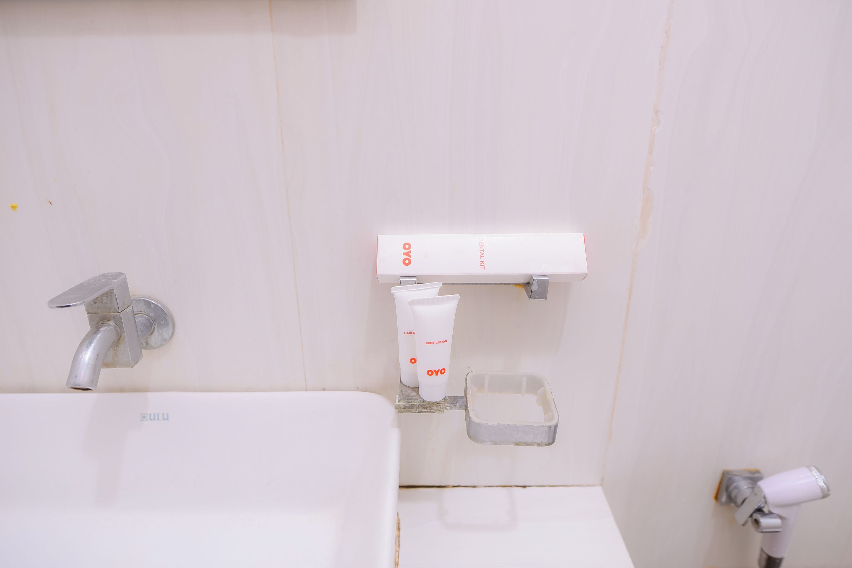 Casa de banho com lavatório branco, torneira, espelho e prateleira com produtos de higiene, incluindo escova de dentes e tubo de loção corporal.