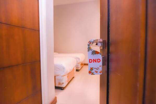 A hotel room with a bed, a bedside table, and a door with a DND sign.