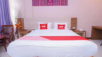 A hotel room with a bed, two pillows with 'OYO' branding, a bedside table with a phone, and a wall with patterned decor.