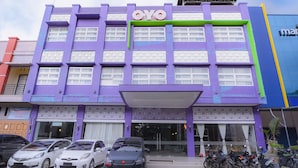 Un immeuble à plusieurs étages, doté d’une façade violette, d’une enseigne « OYO » et de plusieurs voitures et motos garées devant.