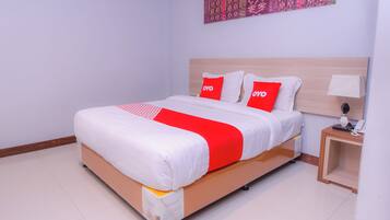 A neatly made bed with a white and red bedspread, two red pillows with "OYO" branding, a bedside table with a lamp, and a wall with a patterned tapestry.