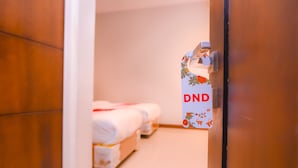 Une chambre d’hôtel avec une porte en bois, un lit recouvert d’une couverture blanche et une pancarte sur laquelle est écrit « Ne pas déranger ».