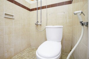 Un box de ducha pequeño y cerrado con inodoro blanco, paredes con azulejos y ducha.