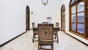 A dining area with a wooden table and chairs, a chandelier, and a view through a large window. - Oyo 2004 Penginapan Bidara Syariah (Probolinggo)