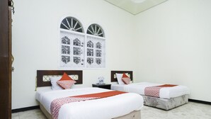 A hotel room with two beds, a window with decorative grills, a wooden headboard, and a tiled floor. - Oyo 2004 Penginapan Bidara Syariah (Probolinggo)