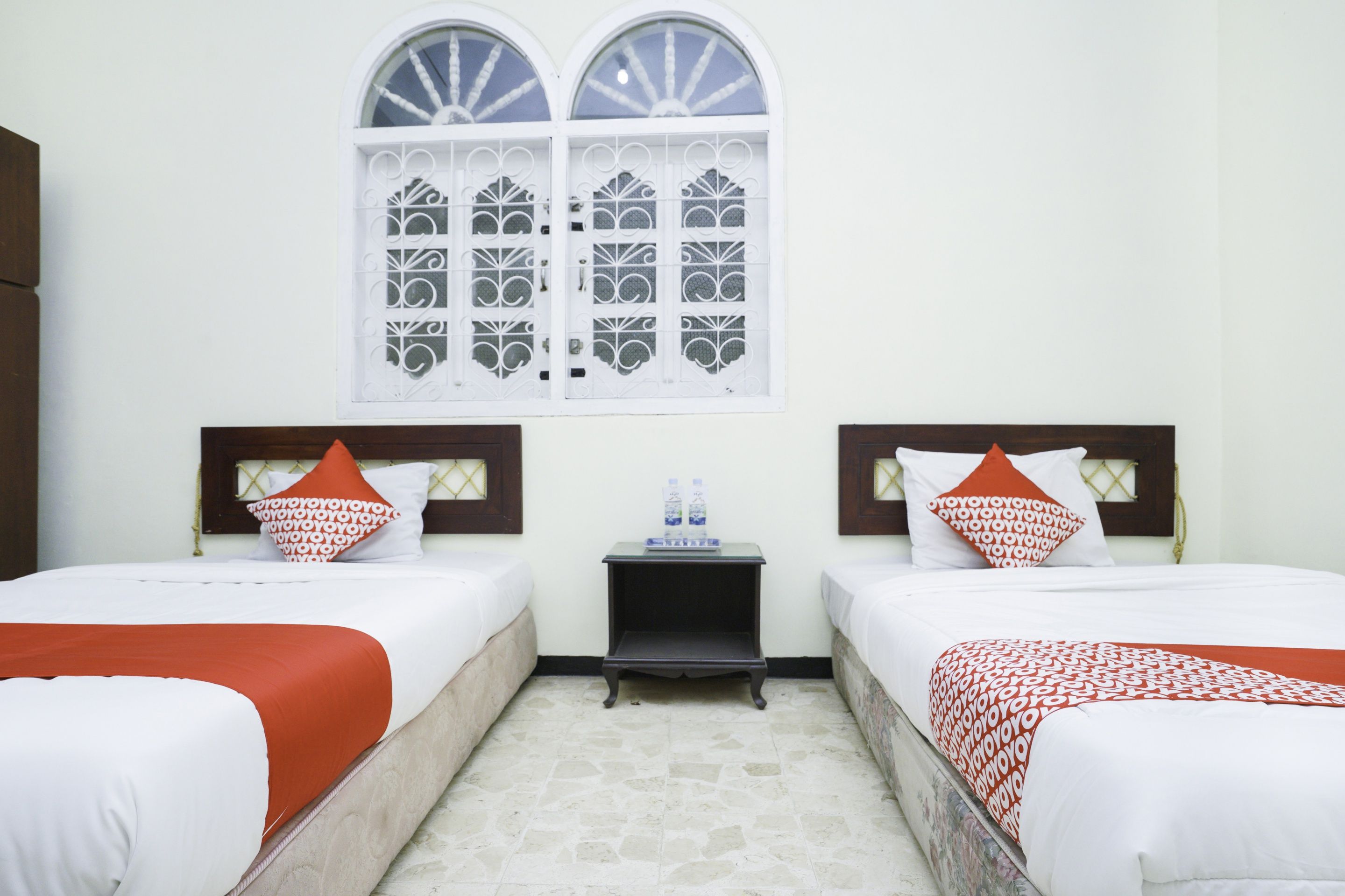 A hotel room with two beds, a small table, and a window with decorative glass.