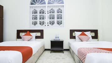 A hotel room with two beds, a small table, and a window with decorative glass.