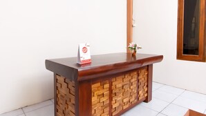 A wooden reception desk with a woven pattern on the lower half, a small potted plant, and a sign on top. - Oyo 1718 Homestay Wak Gobenk (Depok)