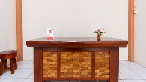 Un mostrador de recepción con acabado de madera y una sección inferior con diseño de ladrillo. Un pequeño jarrón con flores está colocado sobre el mostrador.