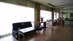 A spacious room with a wooden floor, a sofa, a table, and a chair. There is a large window with curtains, a fireplace, and a mirror on the wall. - OYO 2015 Bandara Hotel Balikpapan (Balikpapan)