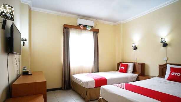 A hotel room with two beds, a TV, an air conditioner, and a desk with a lamp. - OYO 2015 Bandara Hotel Balikpapan (Balikpapan)
