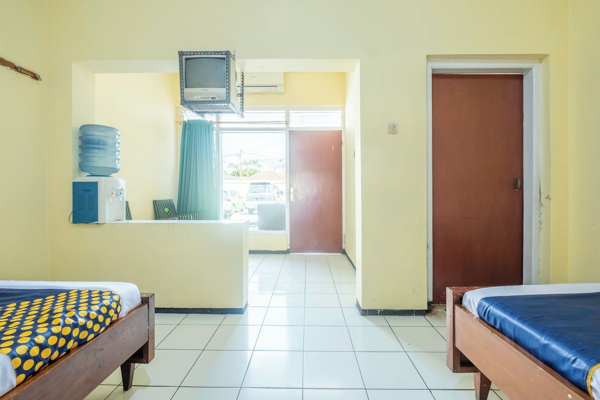 Habitación de hotel con dos camas, televisión, dispensador de agua y vistas al exterior.