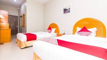 A hotel room with two beds, a wooden headboard, a door, and a framed picture on the wall.