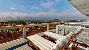 Eine Terrasse mit zwei Liegestühlen und Blick auf Strand und Meer.