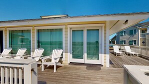Eine Holzterrasse mit weißen Adirondack-Stühlen und einem Glastür-Eingang.