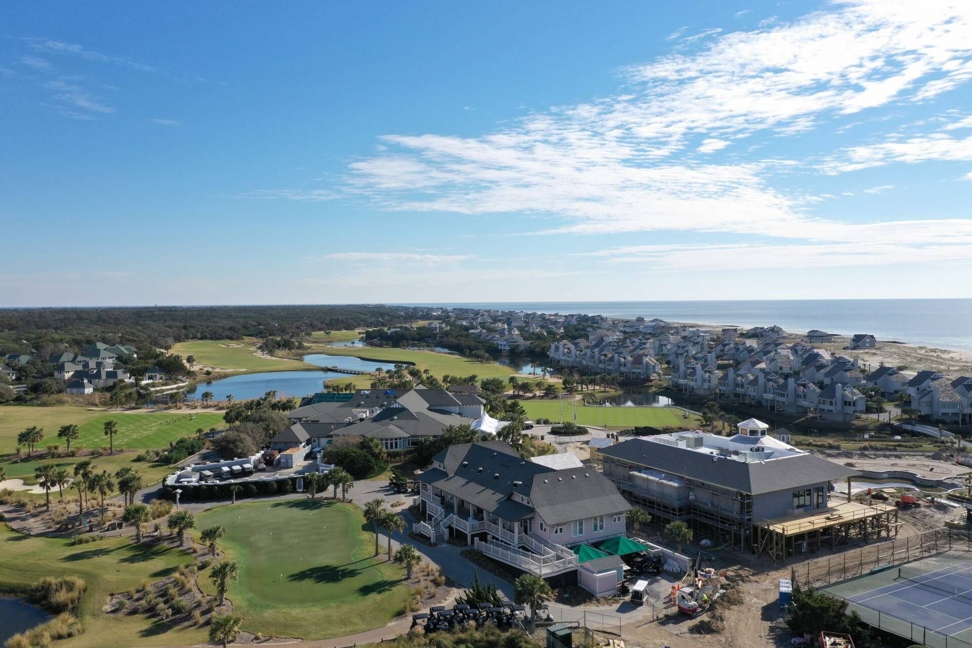 A golf course with a clubhouse, a large body of water, and residential buildings in the background.
