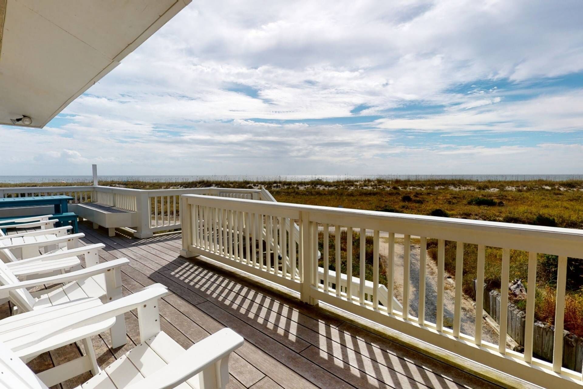 A wooden deck with white railings overlooking a beach with dunes.