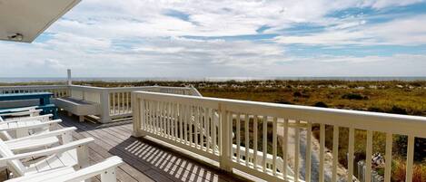 A wooden deck with white railings overlooking a beach with dunes.