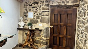 Una habitación con piso de madera, pared de piedra, puerta de madera, mesa de cristal y una planta pequeña.