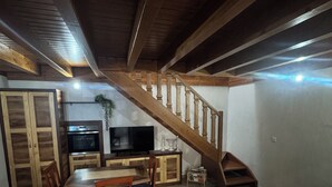 Amplia sala de estar con escalera de madera, una mesa de comedor con sillas, un sofá y un televisor.