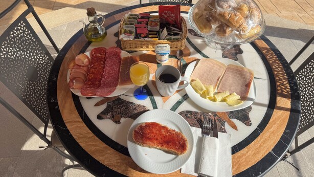 Una mesa redonda con diversos alimentos como embutidos, quesos y pan, acompañados de salsas y un vaso de jugo.
