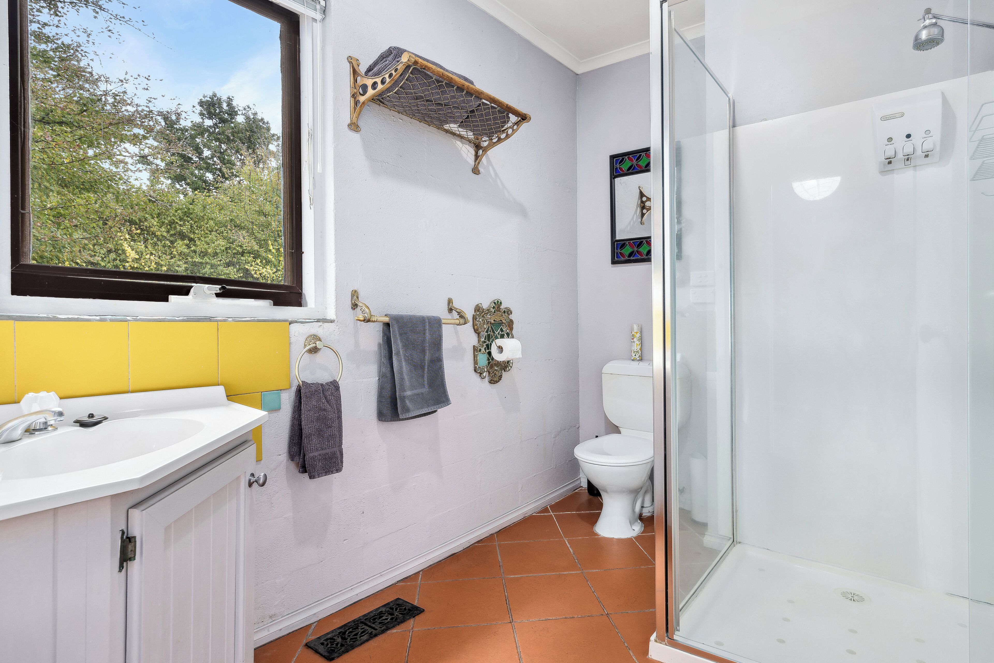 Un baño con lavamanos blanco, pared amarilla, ventana, ducha y retrete.