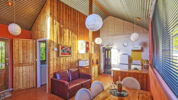 A rustic cabin interior with a wooden interior, a leather sofa, a dining table with chairs, and a kitchen area. - CROFT COTTAGE near Hepburn Mineral Springs Reserve (Hepburn Springs)