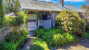 A small, single-story house with a corrugated metal roof, a brick chimney, and a white gate. - CROFT COTTAGE near Hepburn Mineral Springs Reserve (Hepburn Springs)
