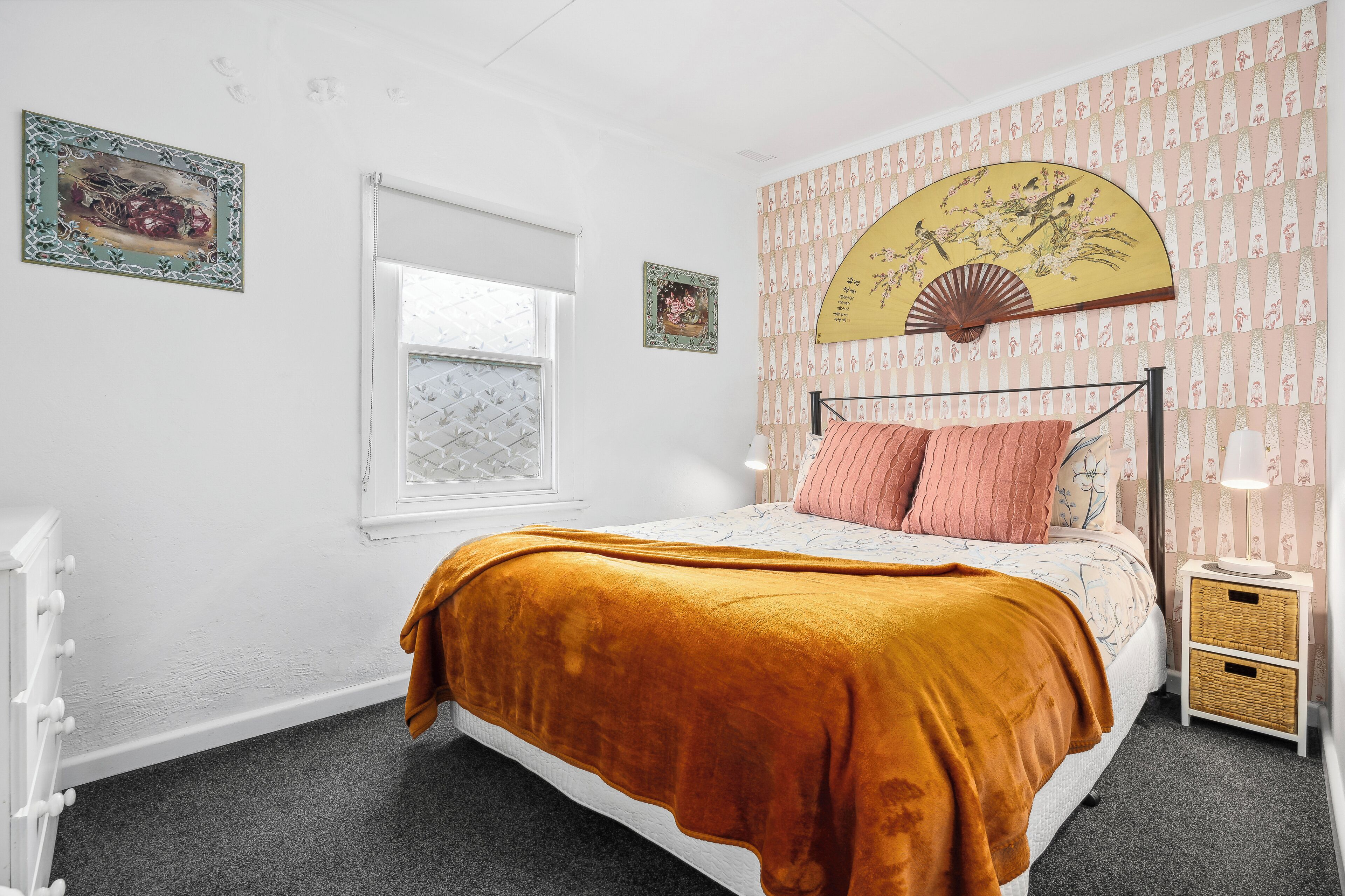 Un dormitorio con cama, ventana, mesita de noche y pared con papel tapiz estampado.