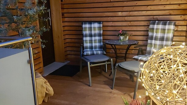 A cozy wooden cabin interior with two plaid chairs, a small round table, and a decorative wicker lamp.